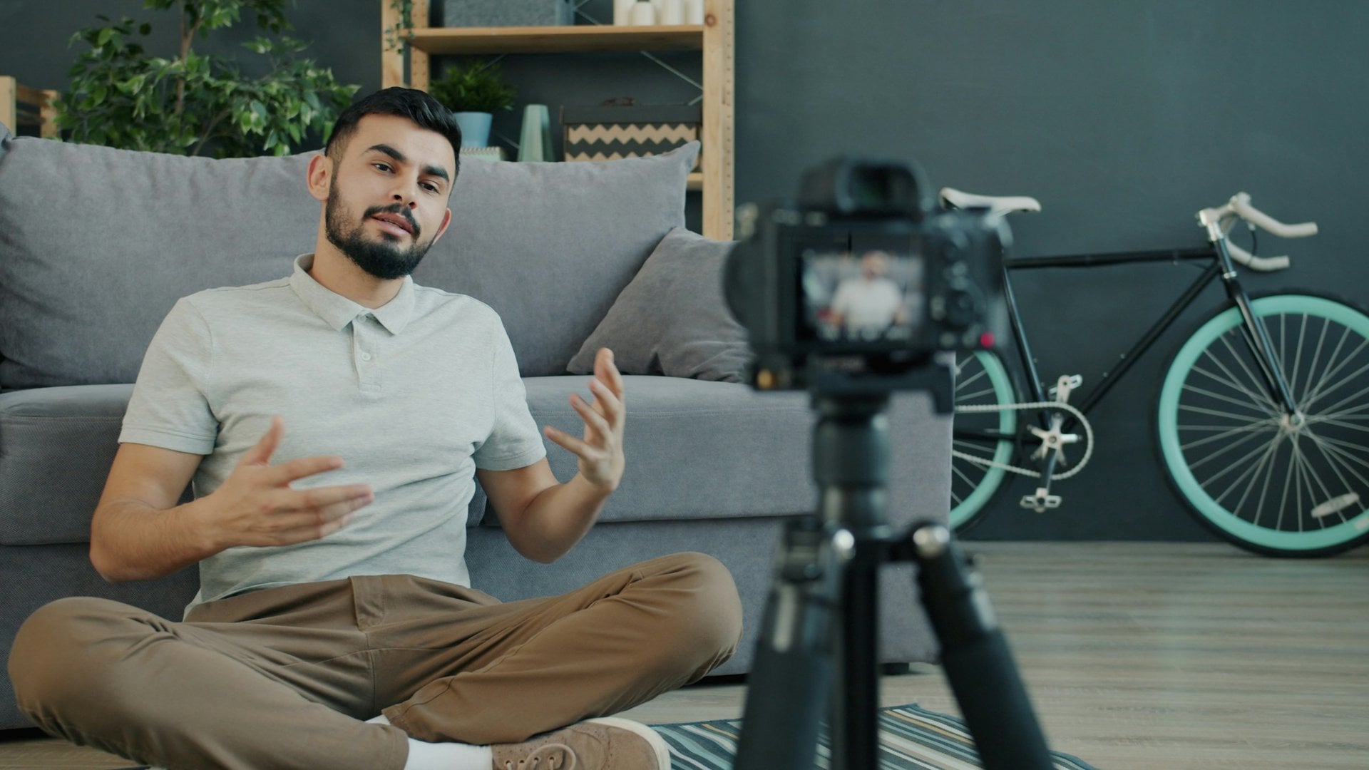 Content creator sitting on the floor talking to a camera on a tripod in a home studio.