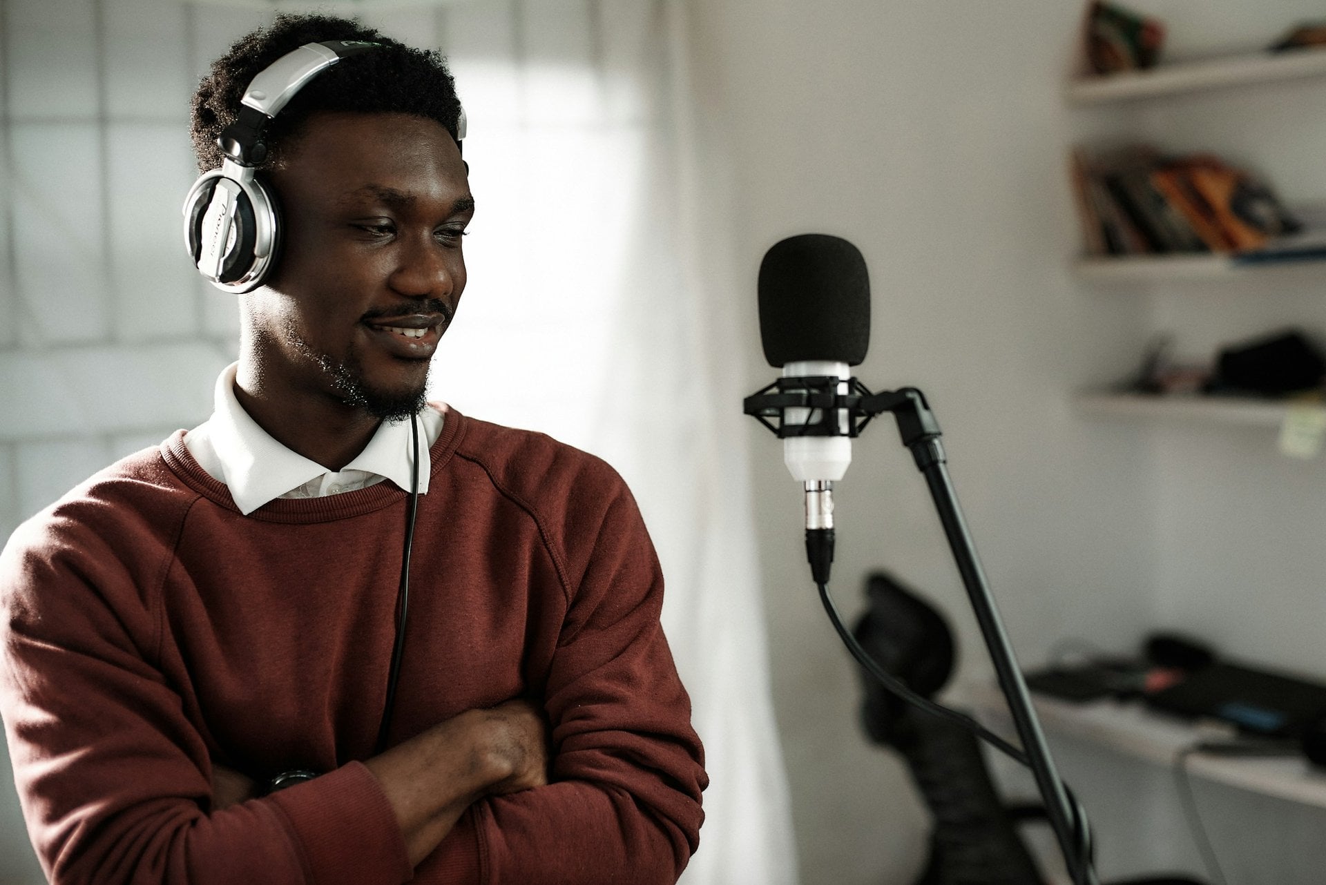 Smiling podcaster wearing headphones beside a studio microphone in a bright home studio.