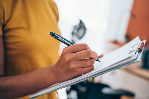 Person in a yellow shirt filling out a form on a clipboard